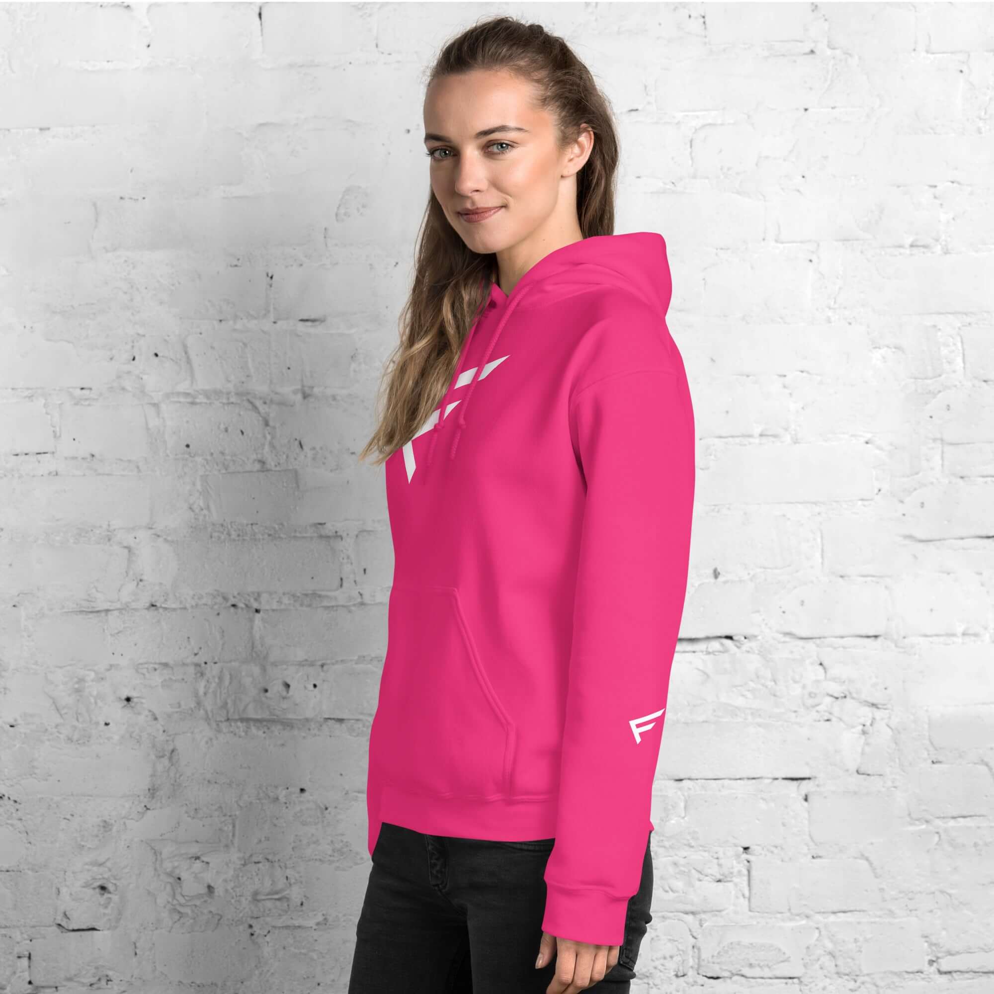 Woman wearing a pink limited-edition hoodie featuring signature 'F' emblem against a brick wall.